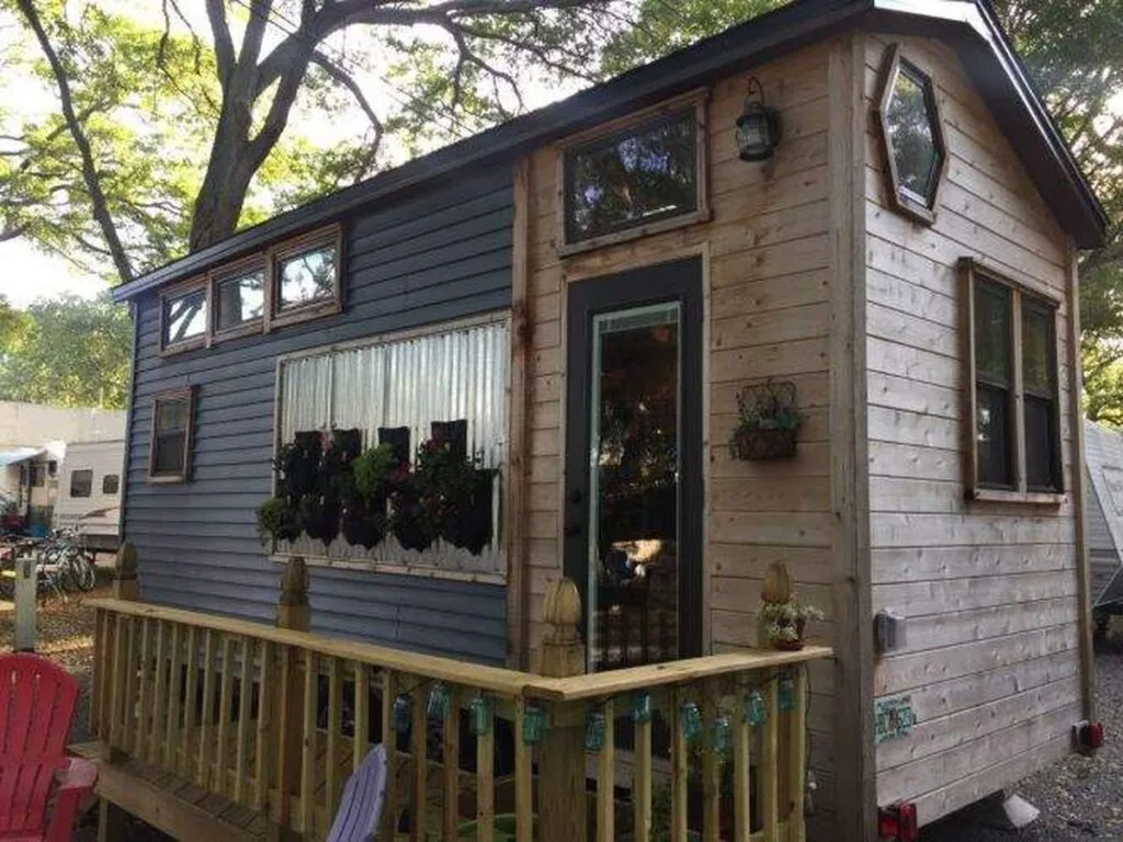 Tiny house on wheels with plants and outdoor seating in a wooded area