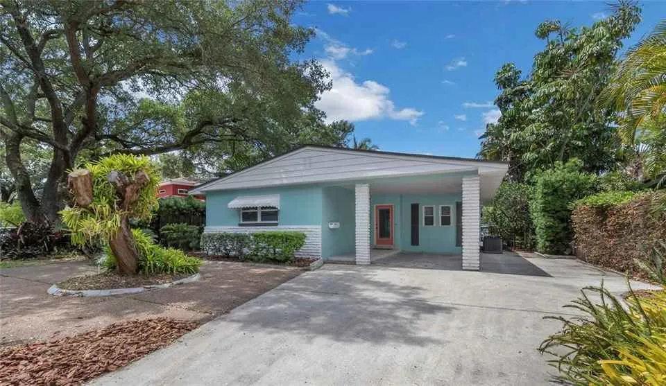 Small pastel blue house with driveway surrounded by trees and plants