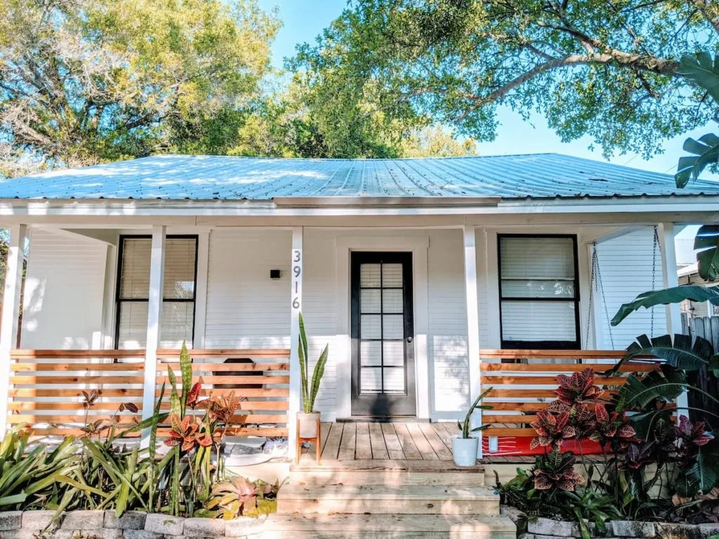 White cottage with a metal roof front porch and lush greenery