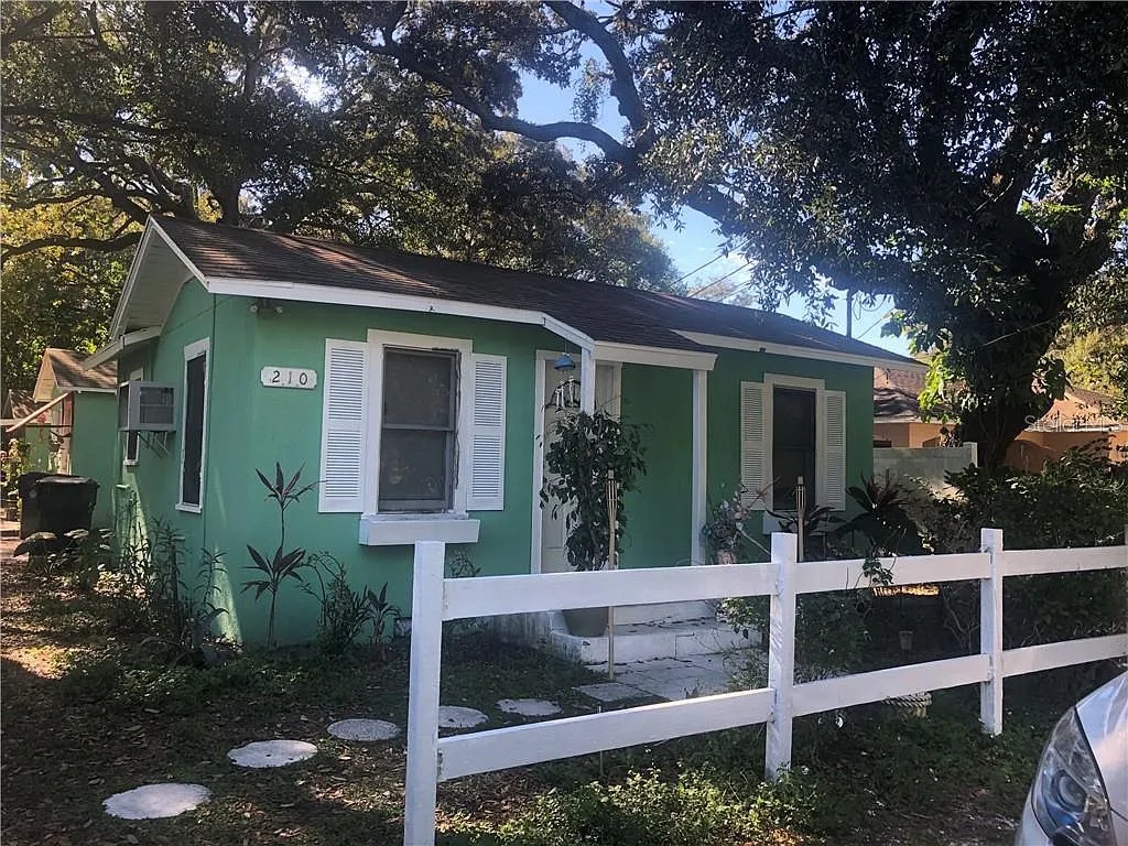 Green cottage with white fence and tree in front yard