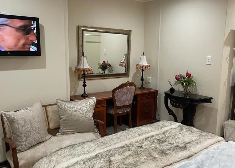 Bedroom with bed desk mirror lamps flowers and wallmounted TV