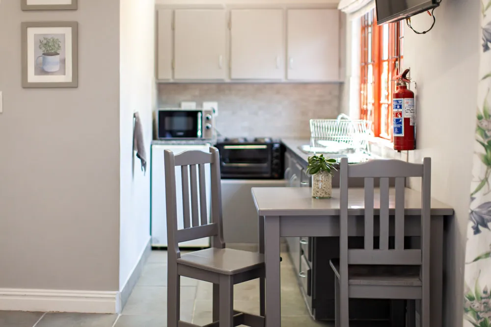 Small kitchen with gray chairs table and appliances wall art and window