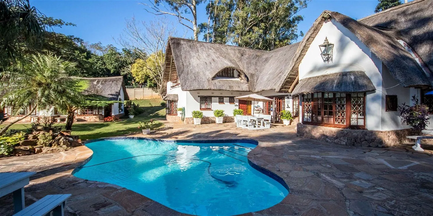 Large house with thatched roof swimming pool and garden in sunny weather