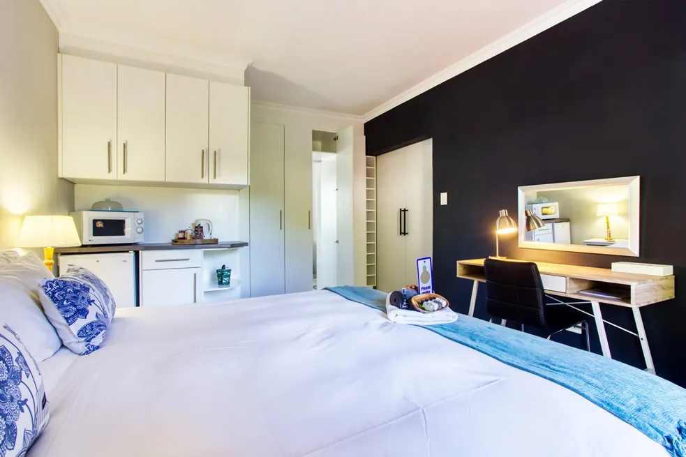 Modern bedroom with white bed kitchenette desk and black accent wall