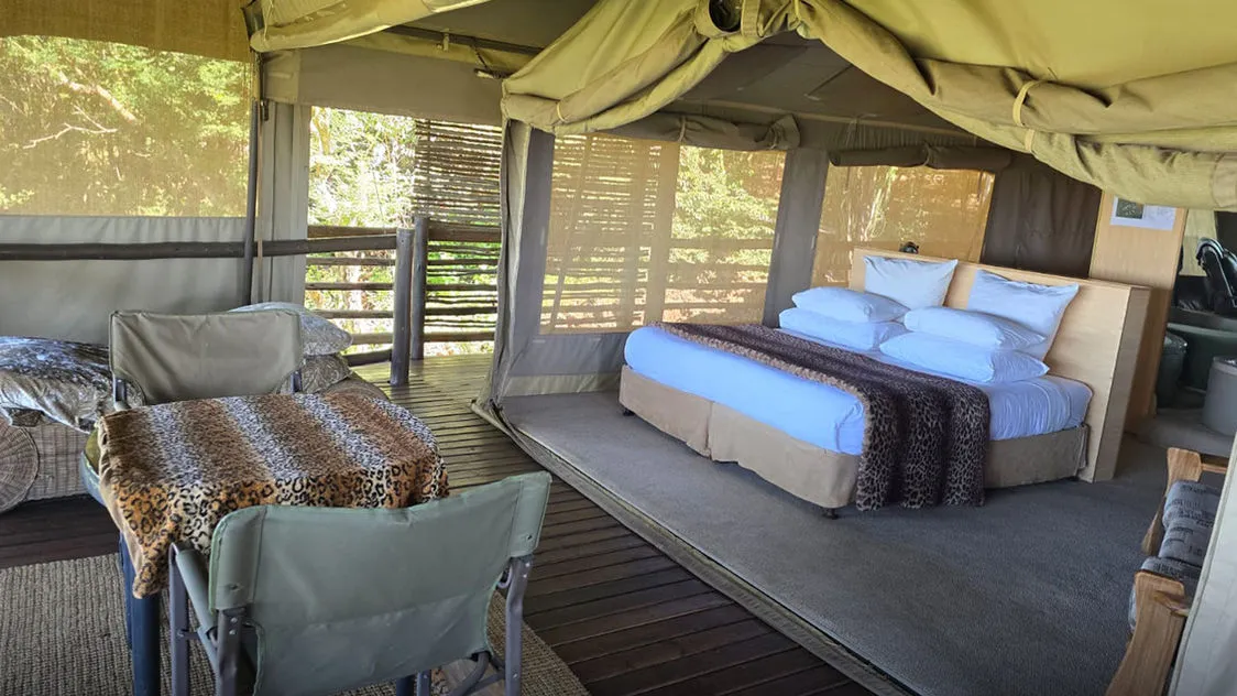 Safari tent interior with bed table and chairs on wooden deck
