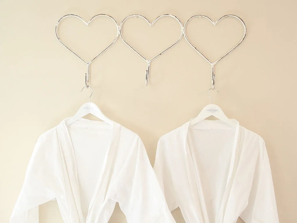 Two white robes hanging on hangers with heartshaped hooks on a beige wall