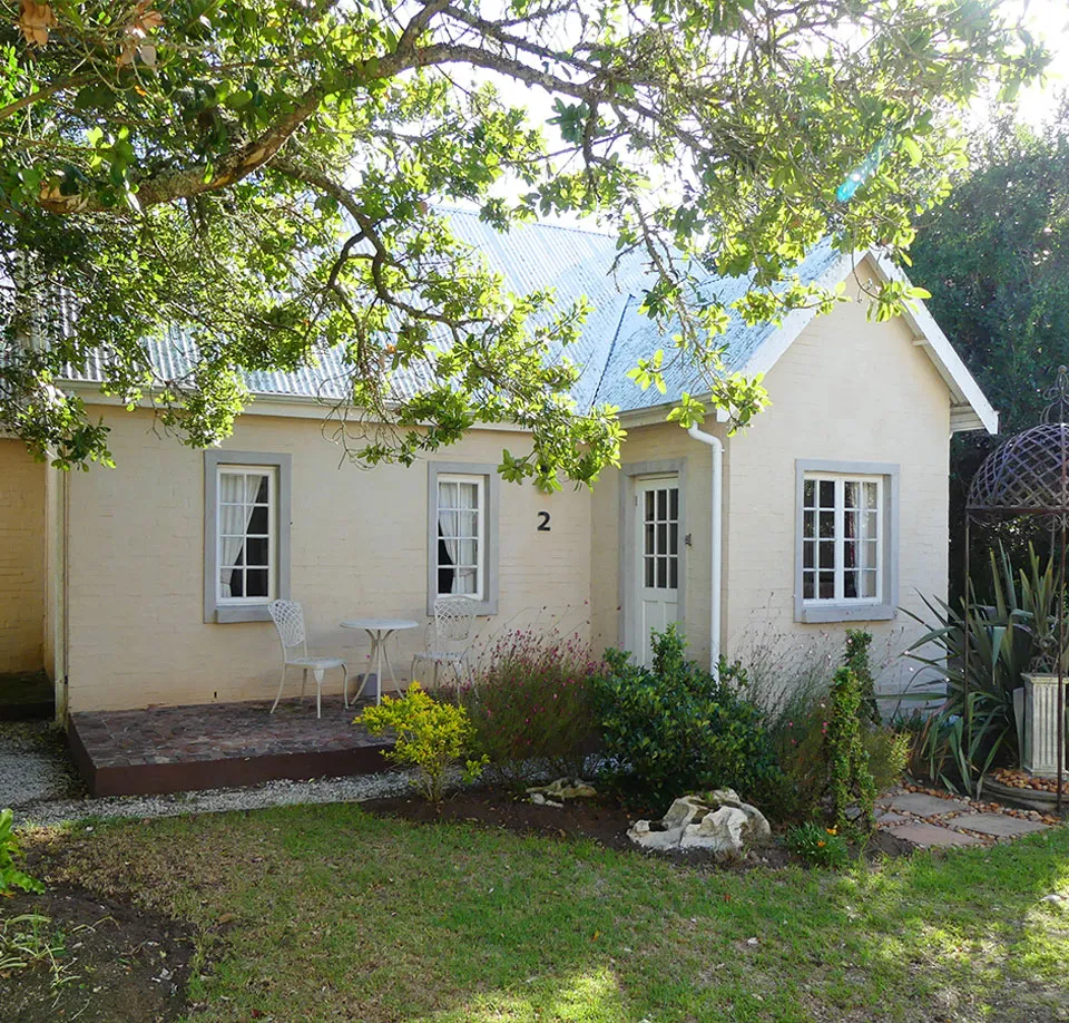 Small yellow cottage with garden patio furniture and overhanging tree branches