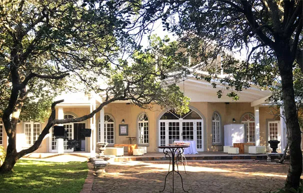 Large house with arched windows and doors surrounded by trees and a paved patio