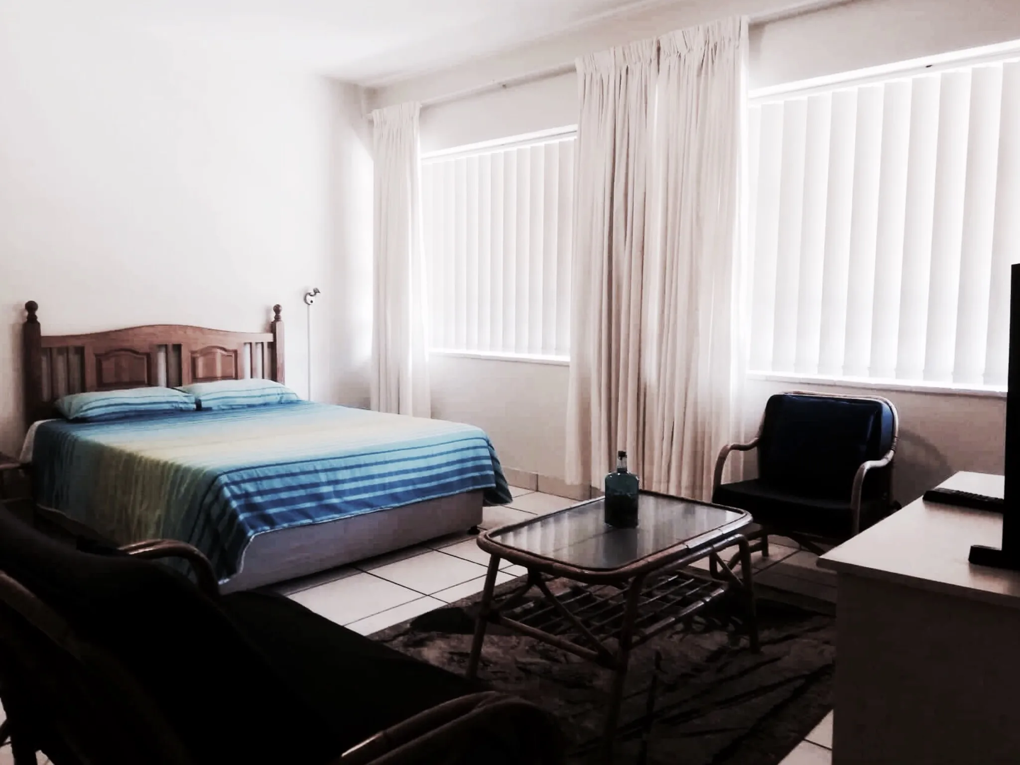 Bedroom with bed armchair TV and window with curtains and blinds