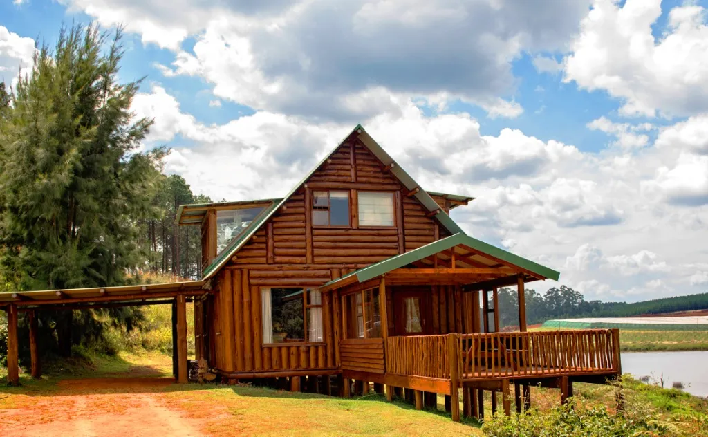 Wooden cabin with green roof by a lake surrounded by trees and grass