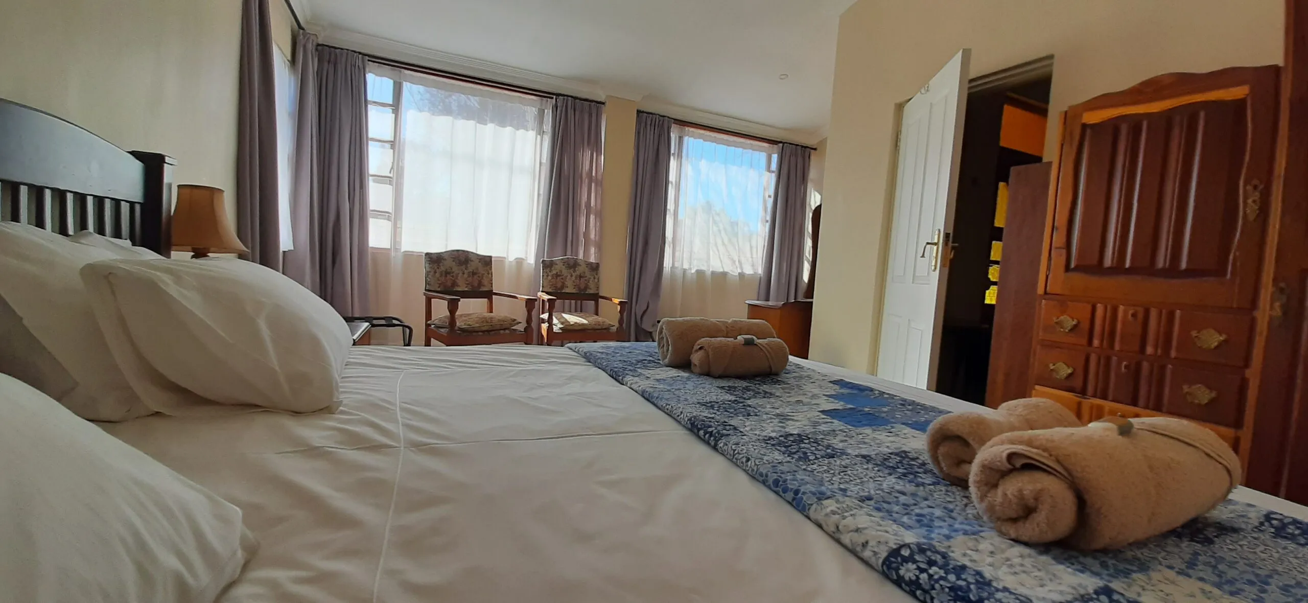 Bedroom with large bed towels chairs and open window with curtains