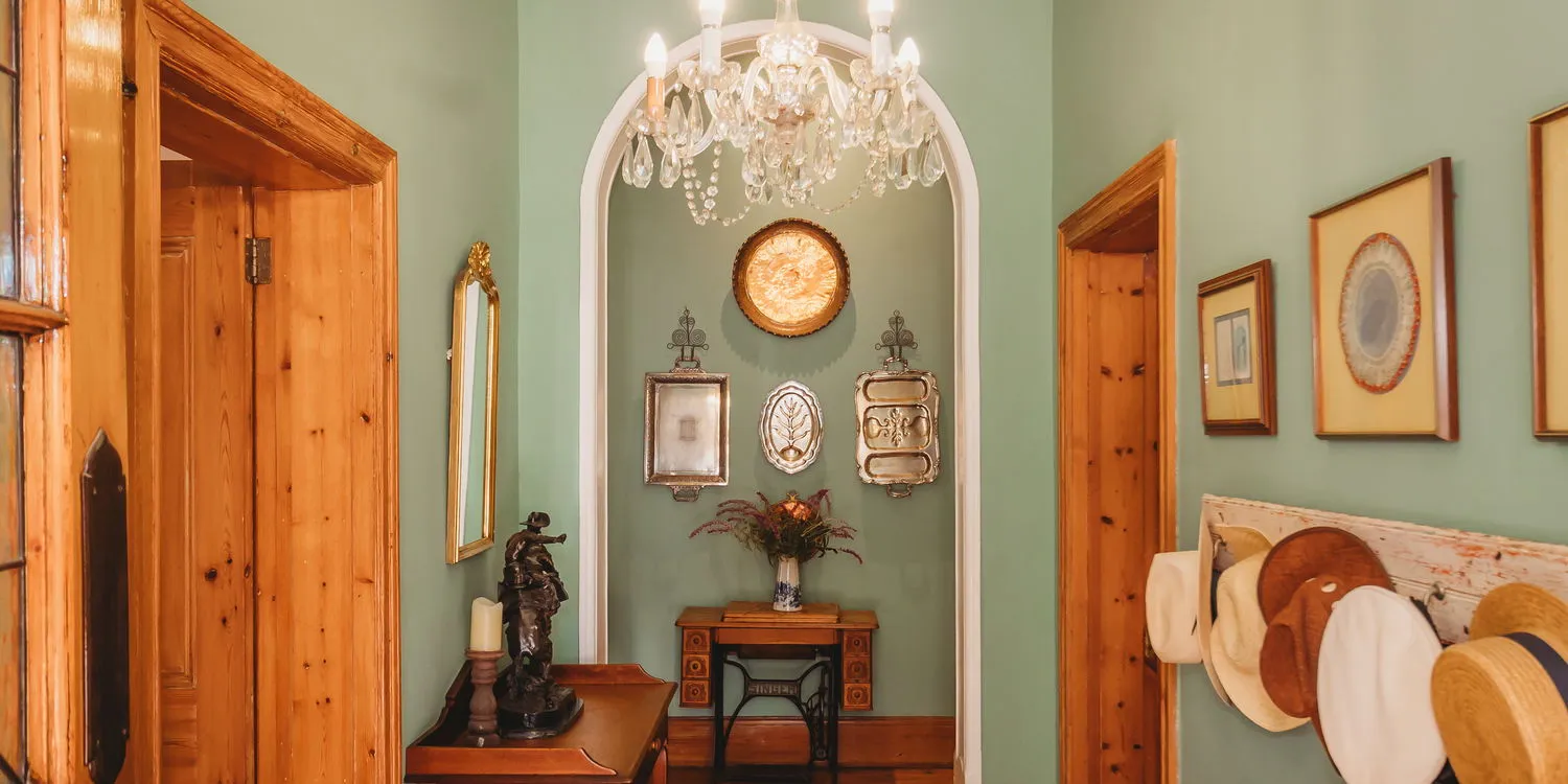 Hallway with wooden doors green walls framed pictures hats and a chandelier