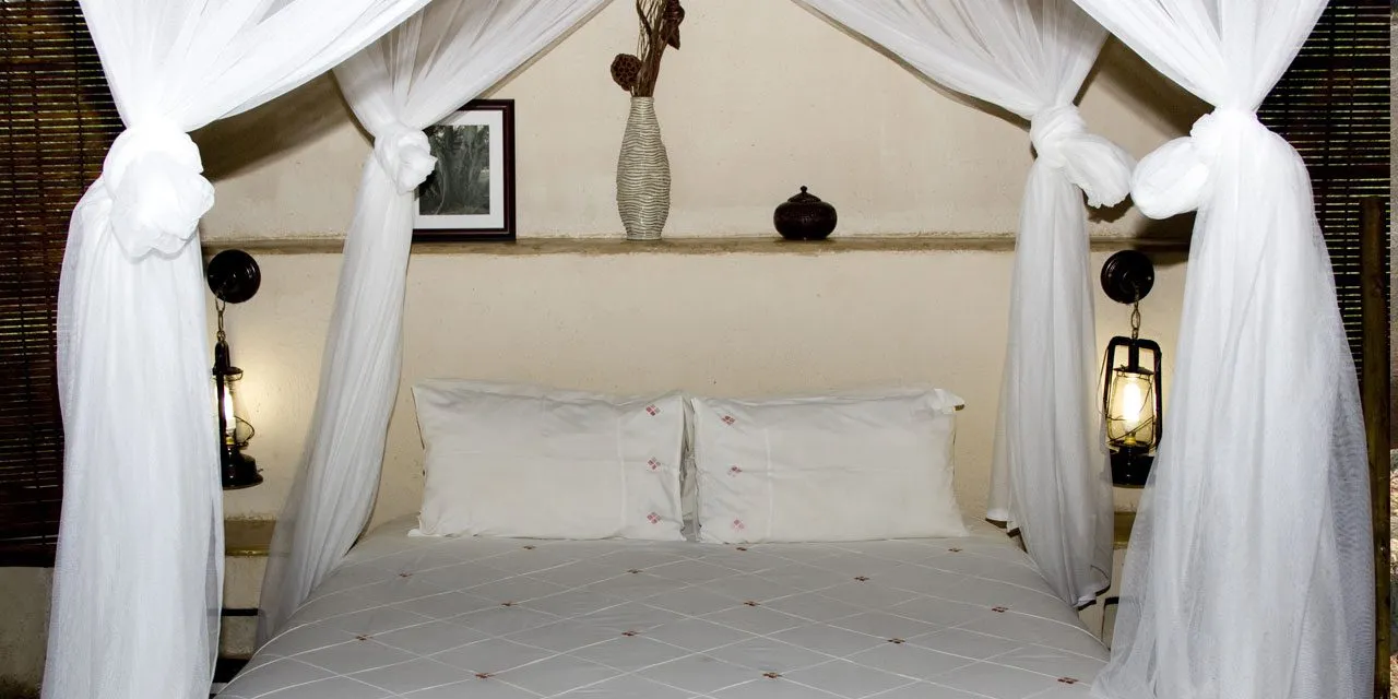Fourposter bed with white canopy pillows and bedside lanterns in a cozy room