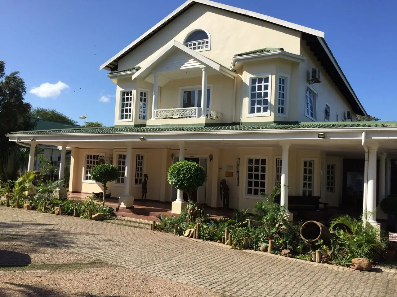 Large twostory house with a veranda surrounded by greenery and potted plants
