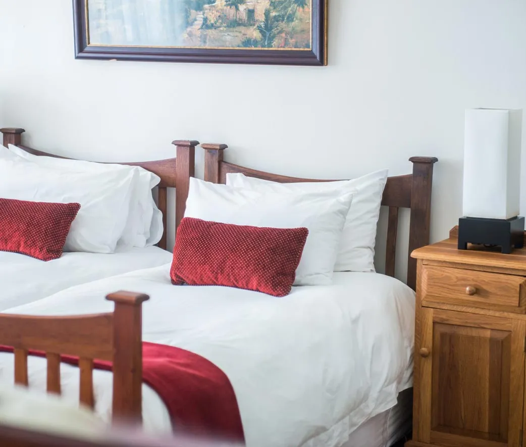 Two beds with red and white pillows wooden headboards and a bedside table with a lamp