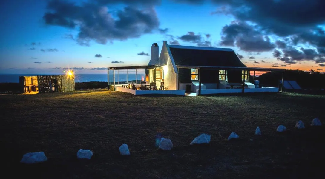 Modern house at dusk with a grassy field and rocks in the foreground