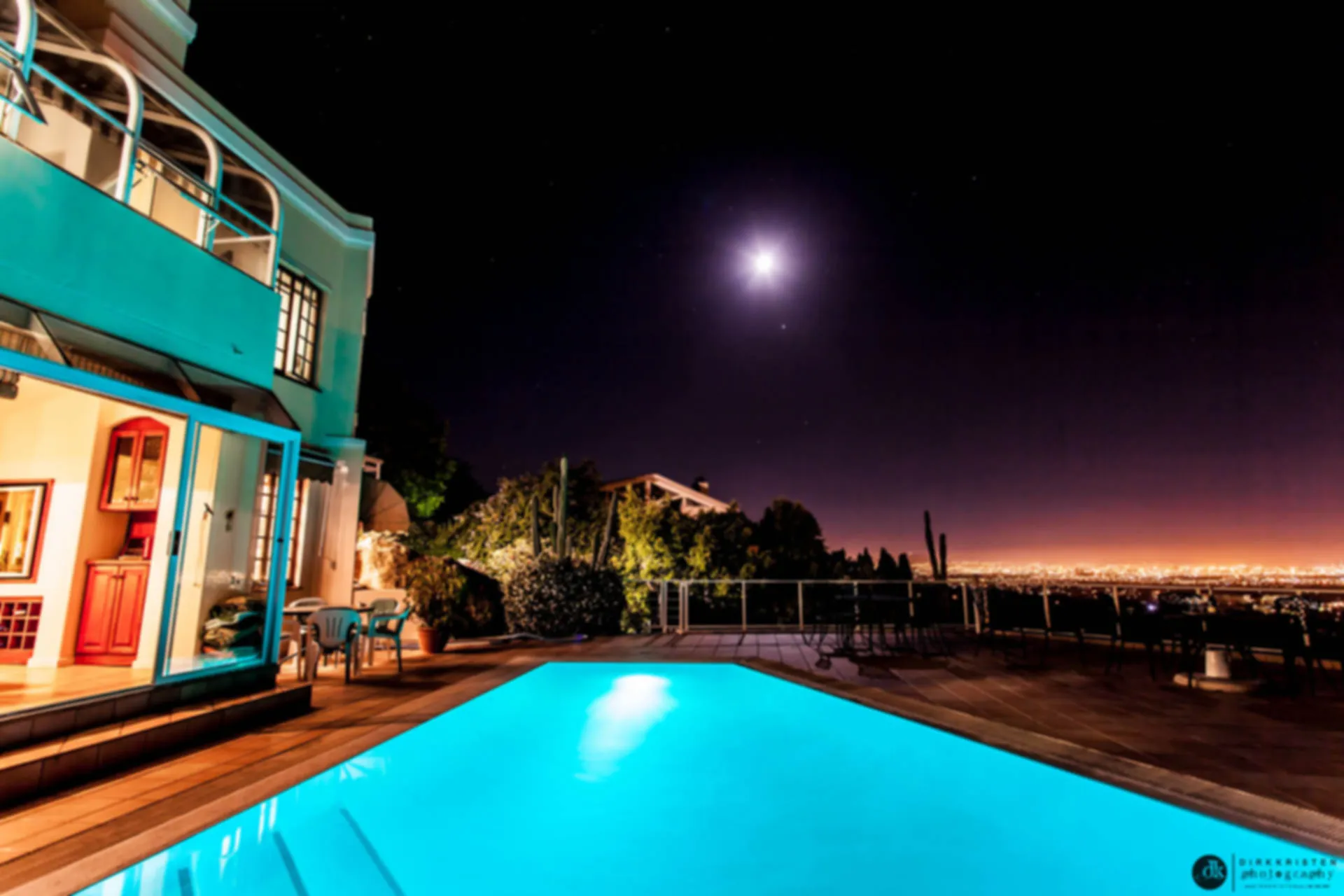Night view of a house with an illuminated pool and city lights in background