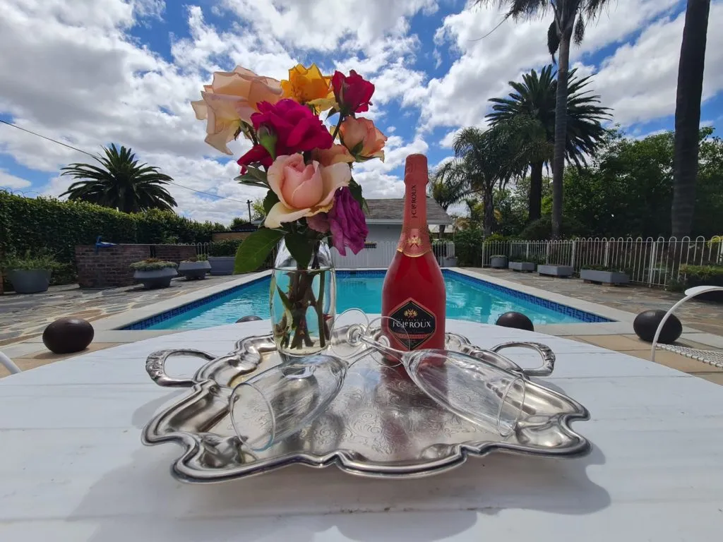 Bottle of sparkling wine and flowers on a tray by a pool