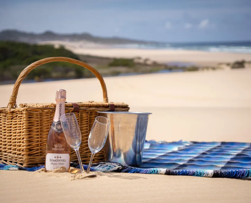 Picnic basket with champagne and glasses on a beach blanket