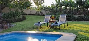 Two lounge chairs by a pool in a lush garden setting