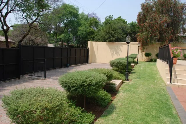 Garden path with black fence green shrubs and a lamppost on a lawn