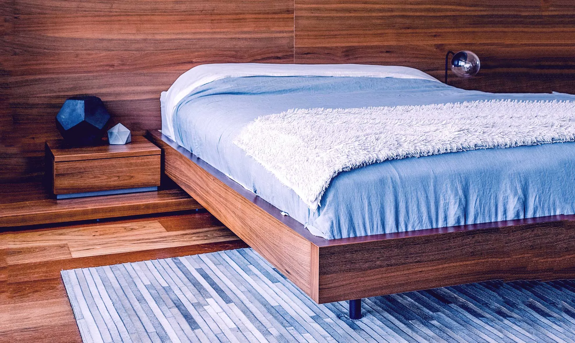 Modern bedroom with wooden bed blue bedding and geometric rug on wooden floor