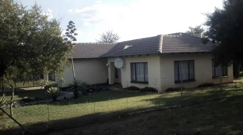Singlestory house with tiled roof and satellite dish surrounded by trees and grass
