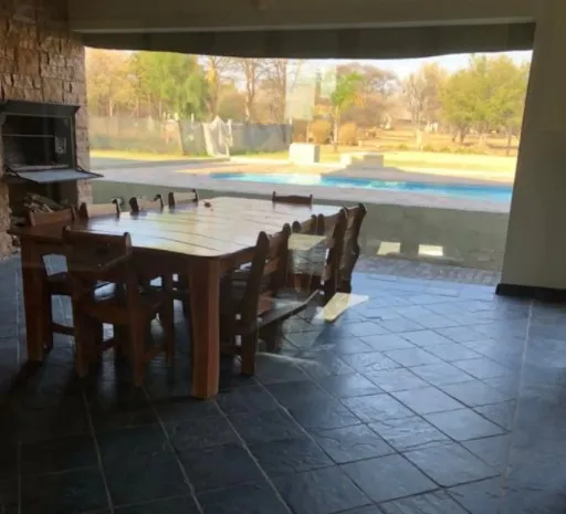 Wooden table and chairs on a patio with a view of a swimming pool