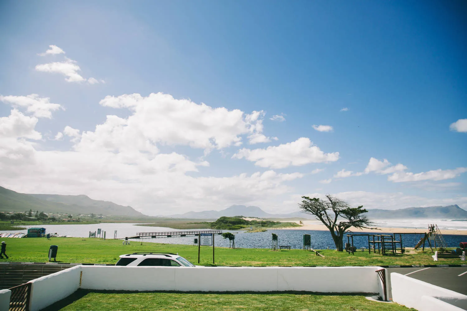 Car parked near a grassy area with ocean and mountains in the background
