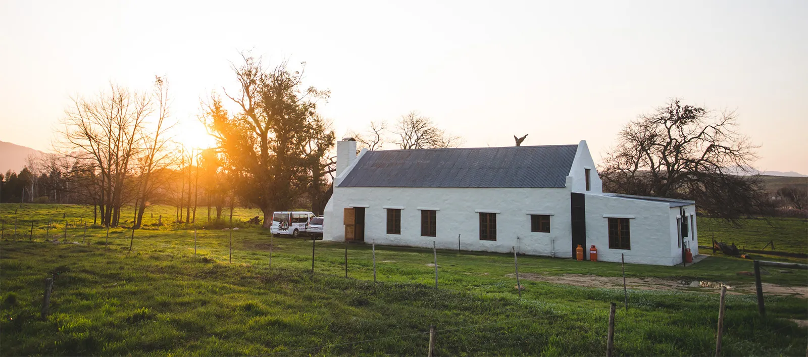 White house on a farm with a sunset in the background and green fields
