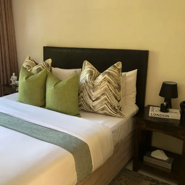 Green and patterned pillows on a bed with a bedside table and lamp