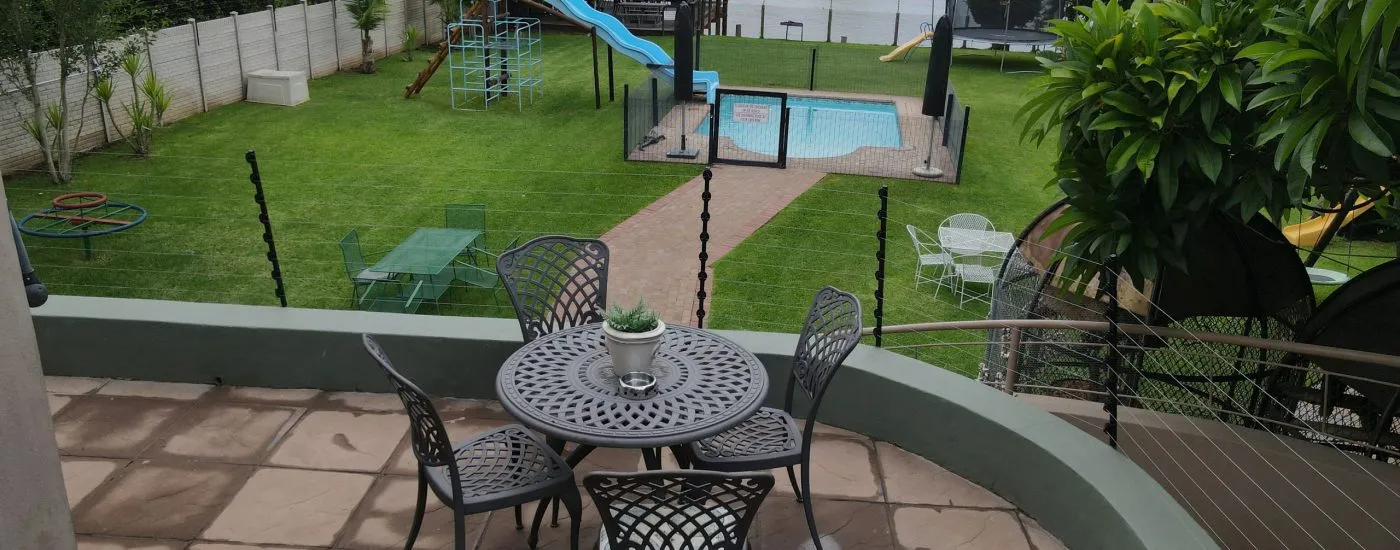 Outdoor seating area with table and chairs overlooking a garden and pool