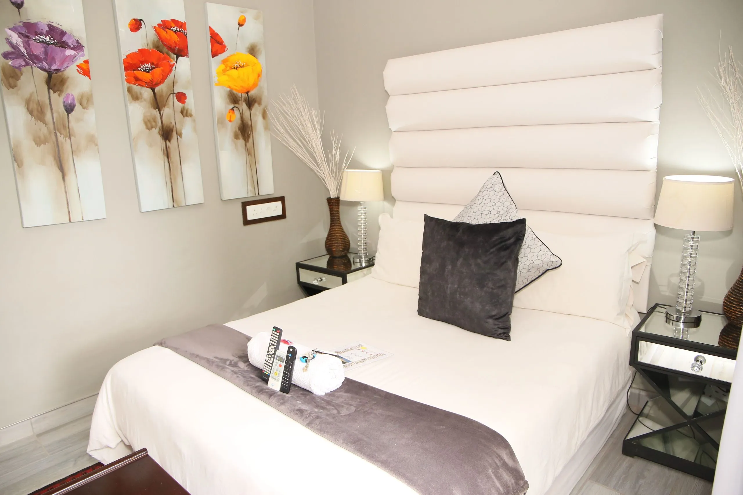Modern bedroom with a large white headboard grey pillows and bedside tables
