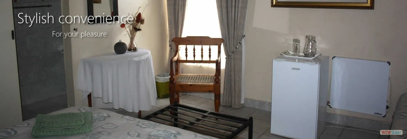 Bedroom with a table chair fridge and bed with a green blanket