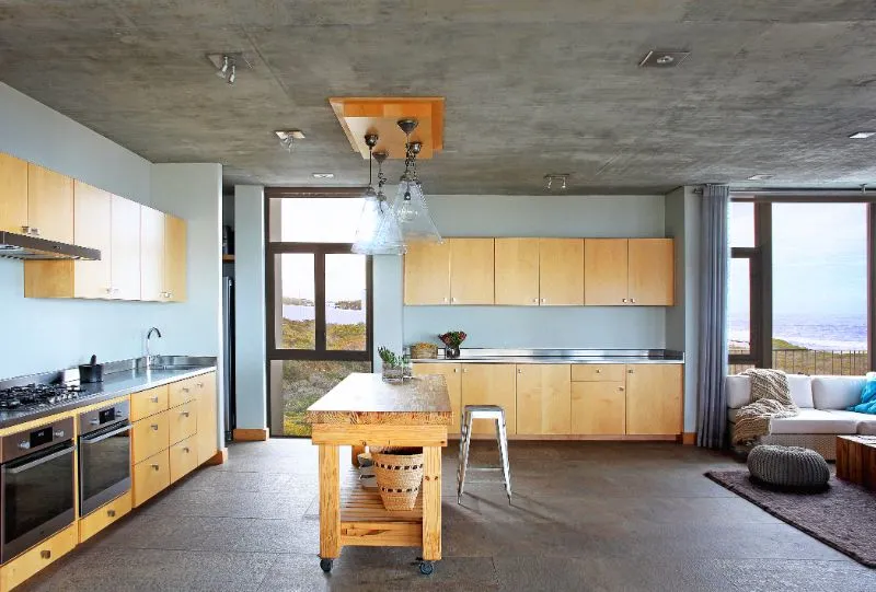 Modern kitchen with wooden cabinets concrete ceiling and large windows overlooking the ocean
