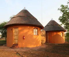 Two traditional huts with thatched roofs in a rural setting at sunset