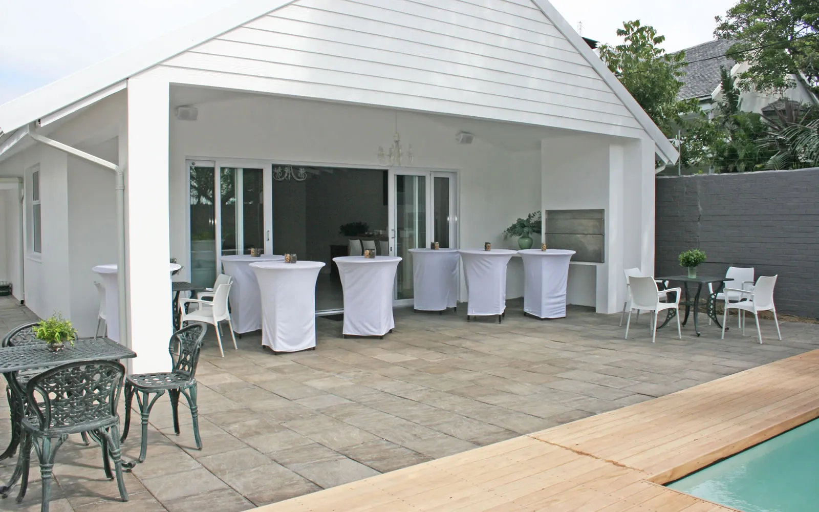 White patio with tables chairs and a poolside wooden deck