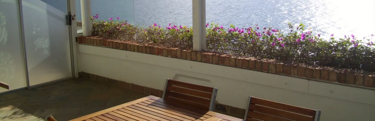 Wooden table and chairs on a patio with a flowerlined view of water