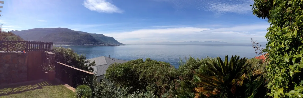 Panoramic view of ocean with greenery and house in foreground mountains in background