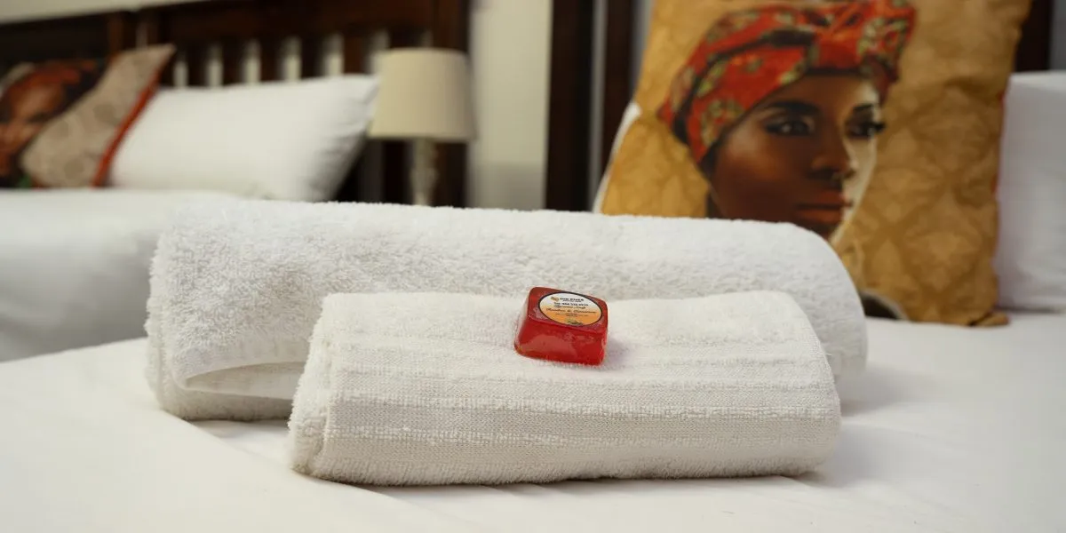 Folded towels with a soap on a bed colorful pillow in the background