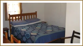 Wooden bed with blue patterned bedspread in a small bedroom with a window
