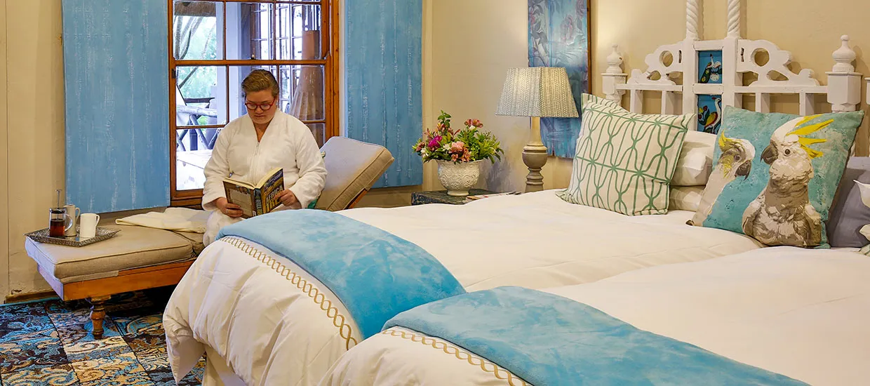 Person reading in a bright decorated bedroom with two beds and blue accents
