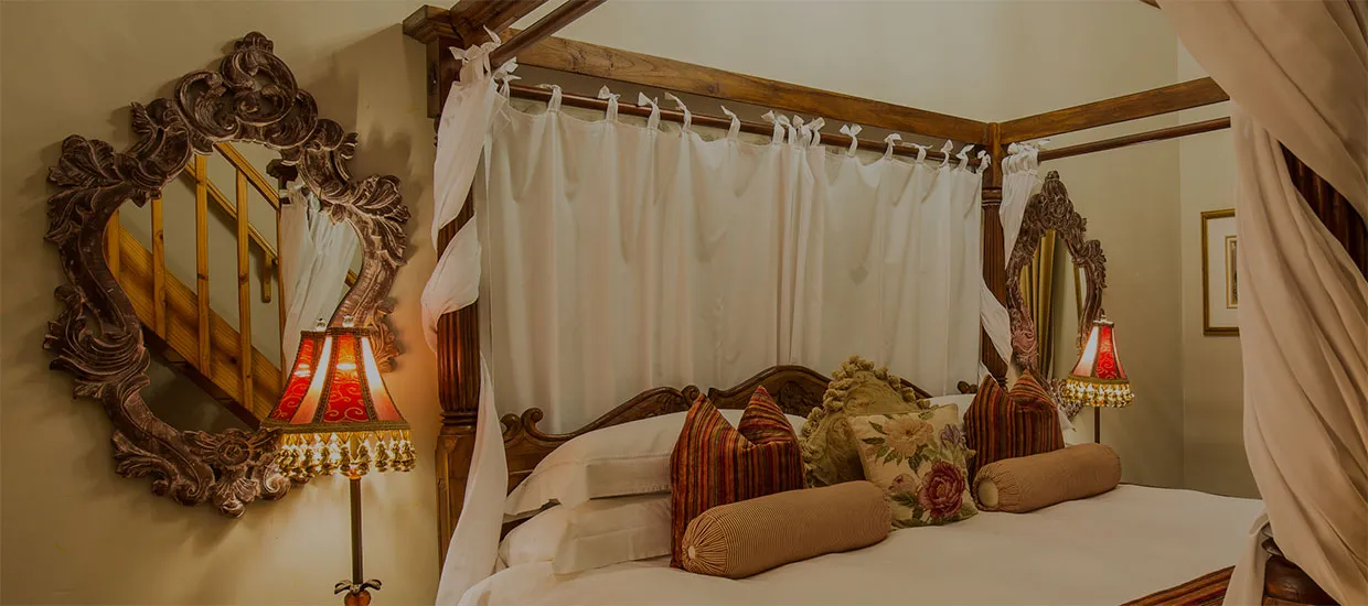Ornate fourposter bed with pillows lamps and mirrors in a cozy bedroom