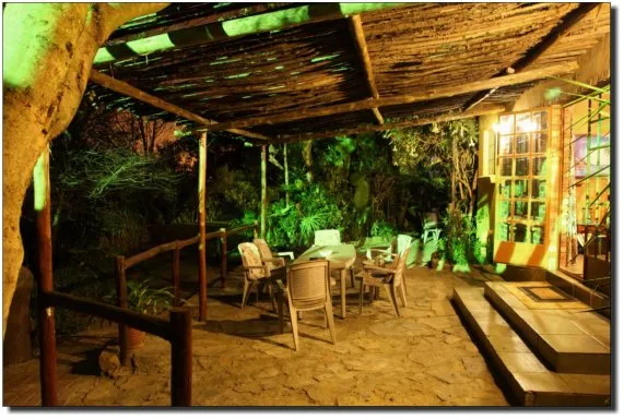 Outdoor seating area with table and chairs under a wooden roof at night