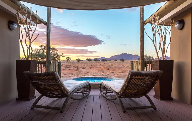 Two wicker chairs on a deck overlooking a desert landscape at sunset