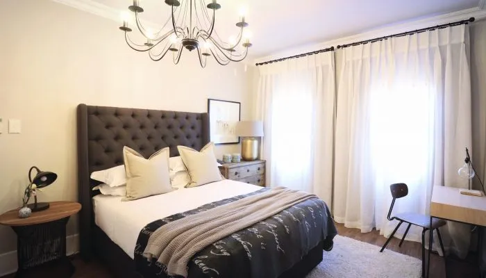 Modern bedroom with large bed nightstand desk and bright windows with curtains