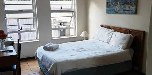 Bright bedroom with a neatly made bed desk and windows