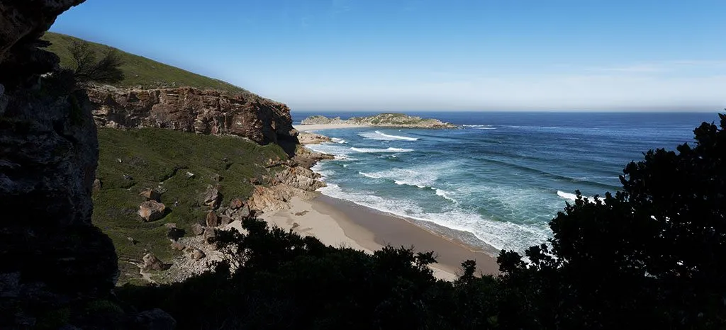 Coastal view with cliffs sandy beach and waves under a clear blue sky