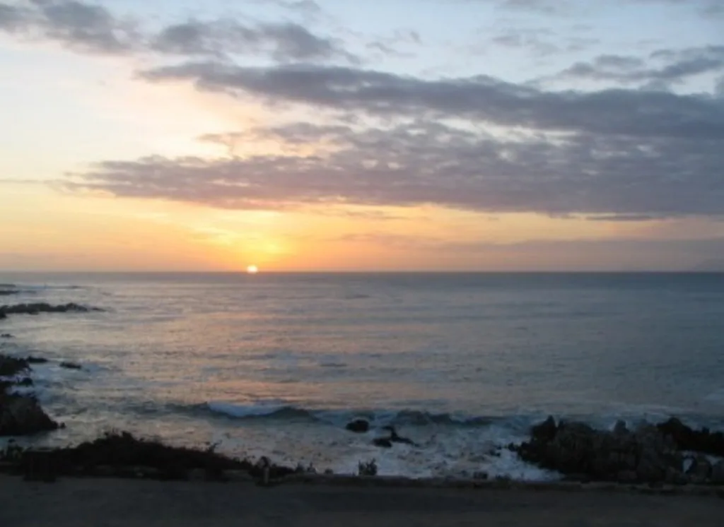 Sunset over the ocean with rocky shoreline in the foreground