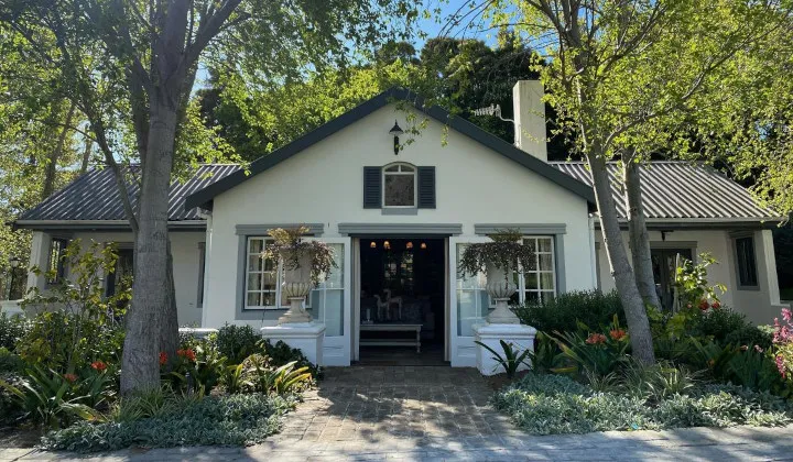 White cottage with open door surrounded by lush greenery and trees